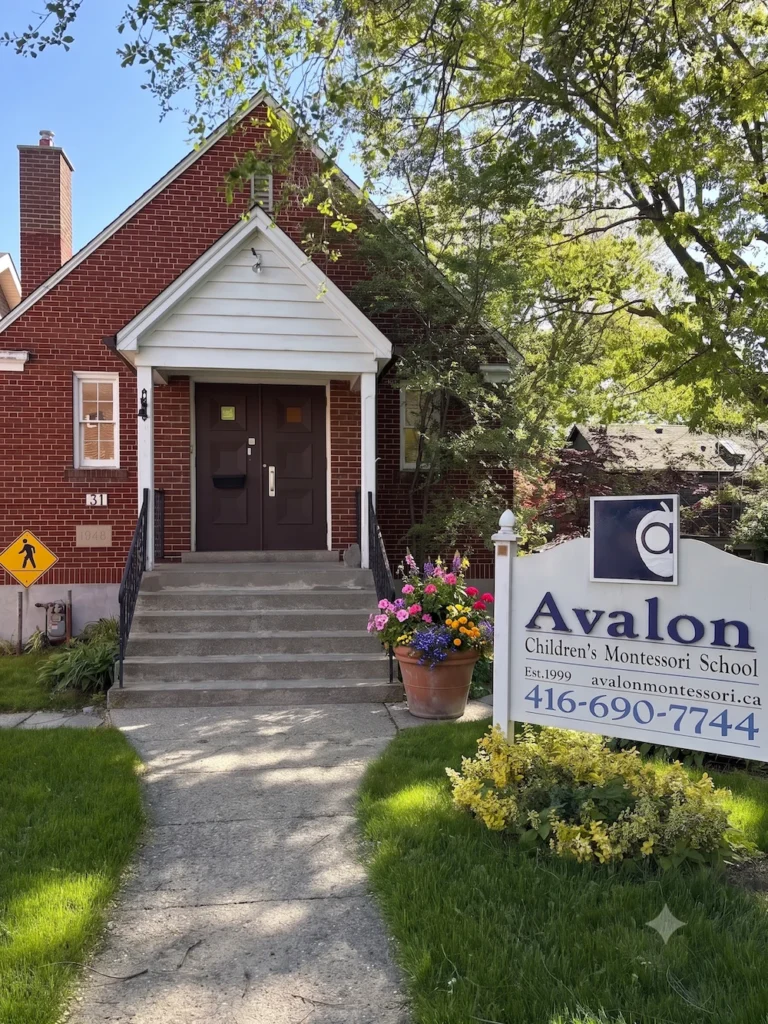 A sign for Avalon Children's Montessori School stands on a lawn in front of a brick building with a concrete walkway.